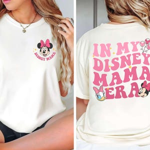 May include: Cream-colored t-shirt featuring Minnie Mouse with a pink bow and the text "Disney Mama." The back of the shirt displays the phrase "In My Disney Mama Era" in pink, along with Daisy Duck, Minnie Mouse, and balloons.