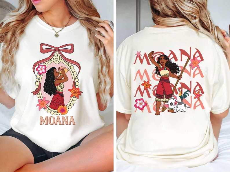 May include: Cream-coloured t-shirt with front and back designs. The front features a cartoon illustration of a woman in a decorative frame with the word "MOANA". The back displays the word "MOANA" repeated with a cartoon character.