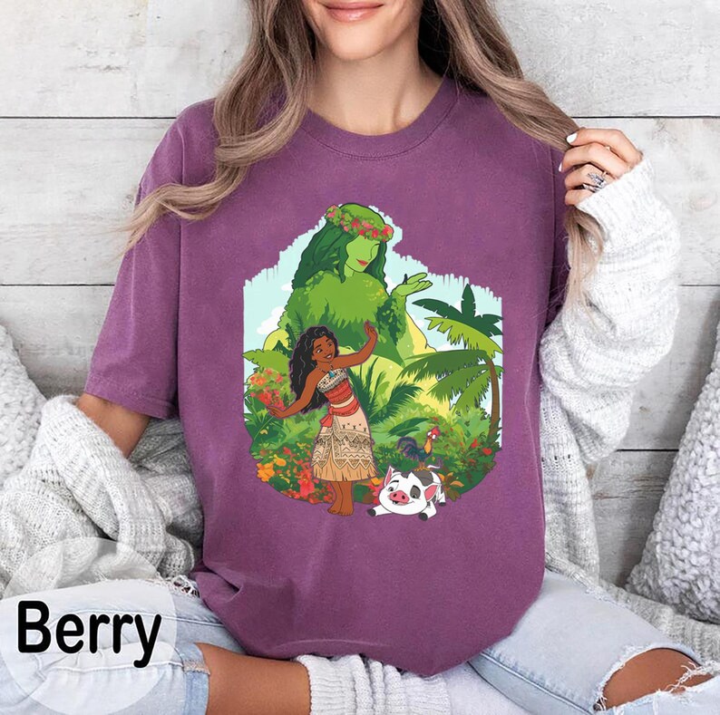 Puede incluir: Camiseta color bayas con un gr&aacute;fico colorido de una mujer con vestimenta tradicional, rodeada de plantas tropicales y un cerdo. El gr&aacute;fico incluye una figura verde y la palabra "Berry" en blanco.