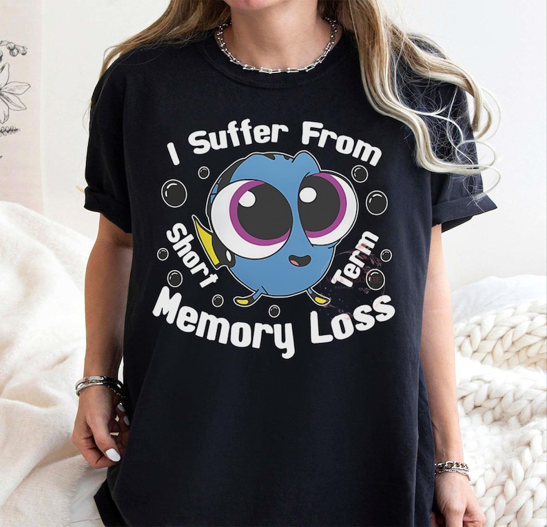 May include: Black t-shirt featuring a cartoon blue fish with large eyes and the text "I Suffer From Short Term Memory Loss." The design includes bubbles around the fish. The shirt is a casual wear item.