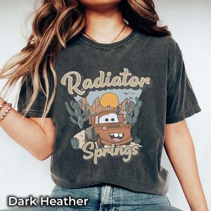 May include: Dark heather grey t-shirt with a vintage-style graphic of a cartoon car in front of a desert landscape. The text "Radiator Springs" is printed on the shirt.