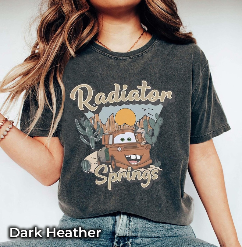 May include: Dark heather grey t-shirt with a vintage-style graphic of a cartoon car in front of a desert landscape. The text "Radiator Springs" is printed on the shirt.
