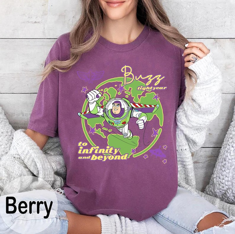 Puede incluir: Camiseta color bayas con un gr&aacute;fico de Buzz Lightyear con un traje espacial verde y blanco, con las palabras "Buzz Lightyear" y "to infinity and beyond". El dise&ntilde;o est&aacute; sobre un gr&aacute;fico de planeta verde y morado.
