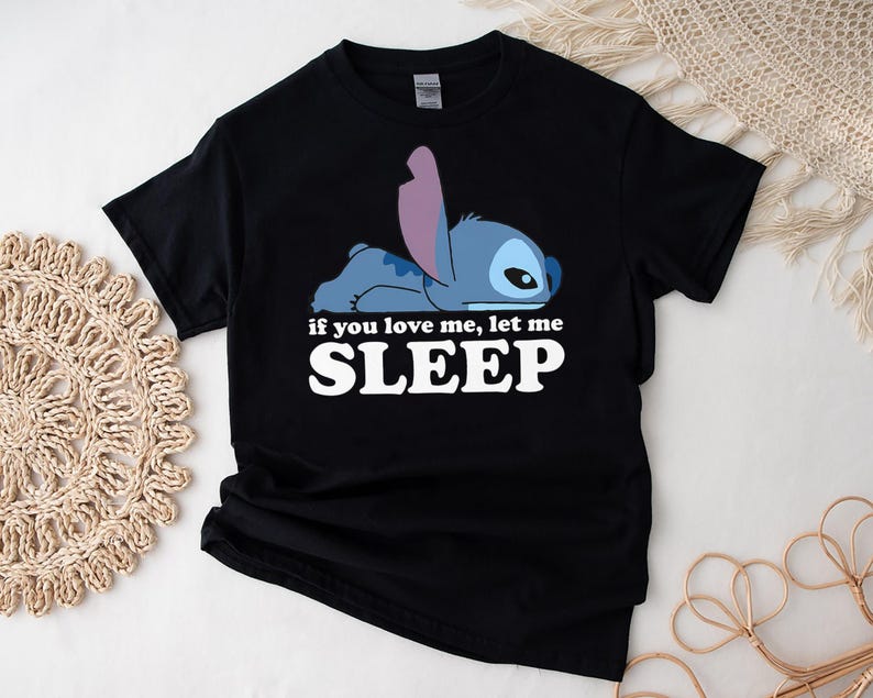 K&ouml;nnte beinhalten: Schwarzes T-Shirt mit einer blauen Stitch-Figur aus Lilo & Stitch. Die Figur liegt mit dem Text "If you love me, let me SLEEP" in wei&szlig; gedruckt.