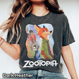 May include: Dark heather gray t-shirt featuring the word "Zootopia" and a colorful graphic of Judy Hopps and Nick Wilde. The shirt is a crew neck and has short sleeves.