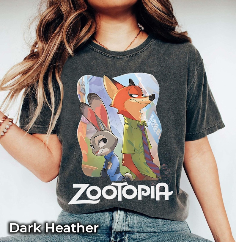 May include: Dark heather gray t-shirt featuring the word "Zootopia" and a colorful graphic of Judy Hopps and Nick Wilde. The shirt is a crew neck and has short sleeves.