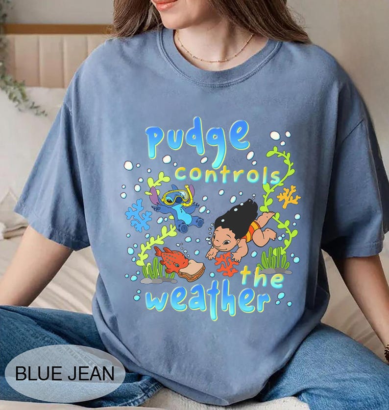 Puede incluir: Camiseta azul vaquero con un gr&aacute;fico de Stitch y Lilo bajo el agua, con el texto "Pudge controls the weather". El dise&ntilde;o incluye personajes de dibujos animados, burbujas y coral.