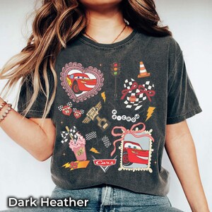 May include: Dark heather t-shirt featuring a Cars-themed graphic. The design includes Lightning McQueen in a heart, checkered flags, a traffic light, and the word "Cars". The shirt has a vintage, worn look.