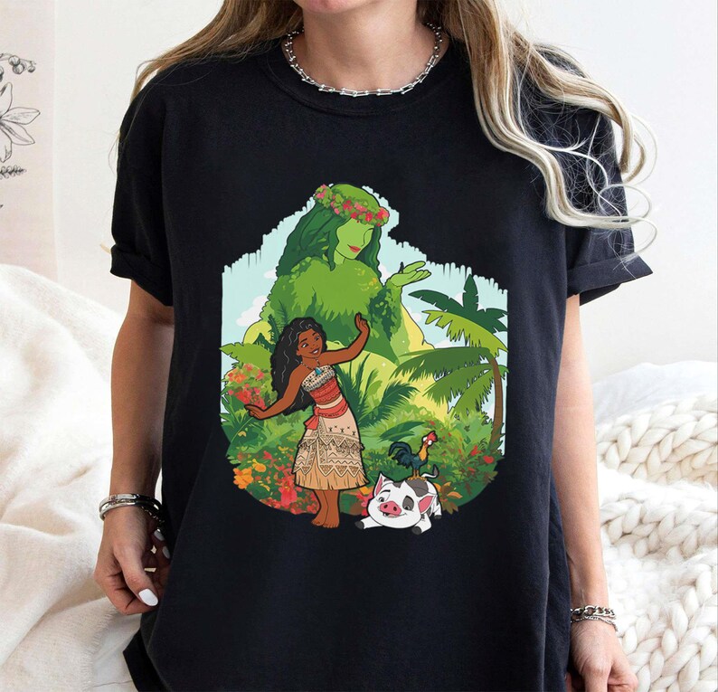 Puede incluir: Camiseta negra con un gr&aacute;fico colorido de una mujer polinesia, una diosa verde, un gallo y un cerdo. El dise&ntilde;o est&aacute; ambientado en un tel&oacute;n de fondo tropical con palmeras y flores. La obra de arte es vibrante y detallada, perfecta para los fan&aacute;ticos de la pel&iacute;cula animada.