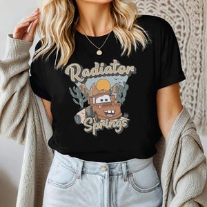 May include: Black t-shirt with a cartoon image of Mater from Cars. The image is surrounded by cacti and the text "Radiator Springs".