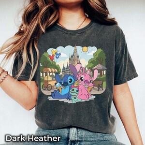 K&ouml;nnte beinhalten: Dunkelgraues Heather-T-Shirt mit einem farbenfrohen Motiv von Stitch und Angel, die Eis vor einem Schloss genie&szlig;en. Das Design umfasst einen Essenswagen, Luftballons und den Text "Dark Heather" unten.