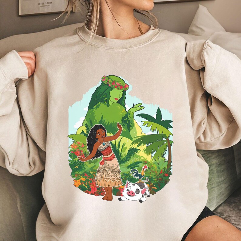 Puede incluir: Sudadera beige con un gr&aacute;fico colorido de una mujer con vestimenta tradicional, una figura verde y plantas tropicales. Un gallo y un cerdo tambi&eacute;n est&aacute;n en el dise&ntilde;o. La sudadera tiene mangas largas y cuello redondo.