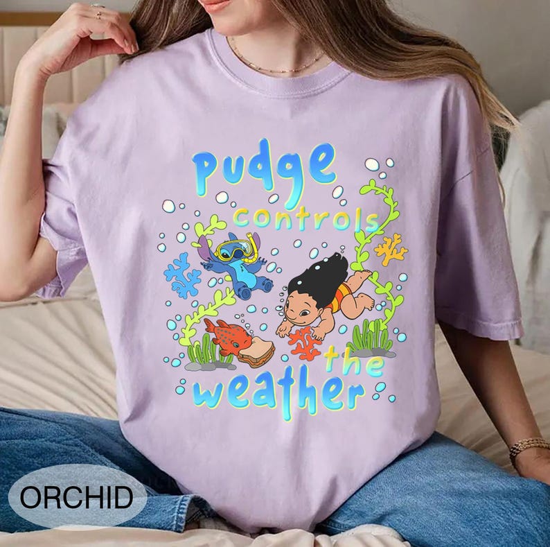 Puede incluir: Camiseta de color lila claro con un dise&ntilde;o de dibujos animados. El dise&ntilde;o presenta el texto "pudge controls the weather" con los personajes Stitch y Lilo, adem&aacute;s de criaturas marinas y burbujas. La camiseta est&aacute; etiquetada "ORCHID" en la parte inferior.