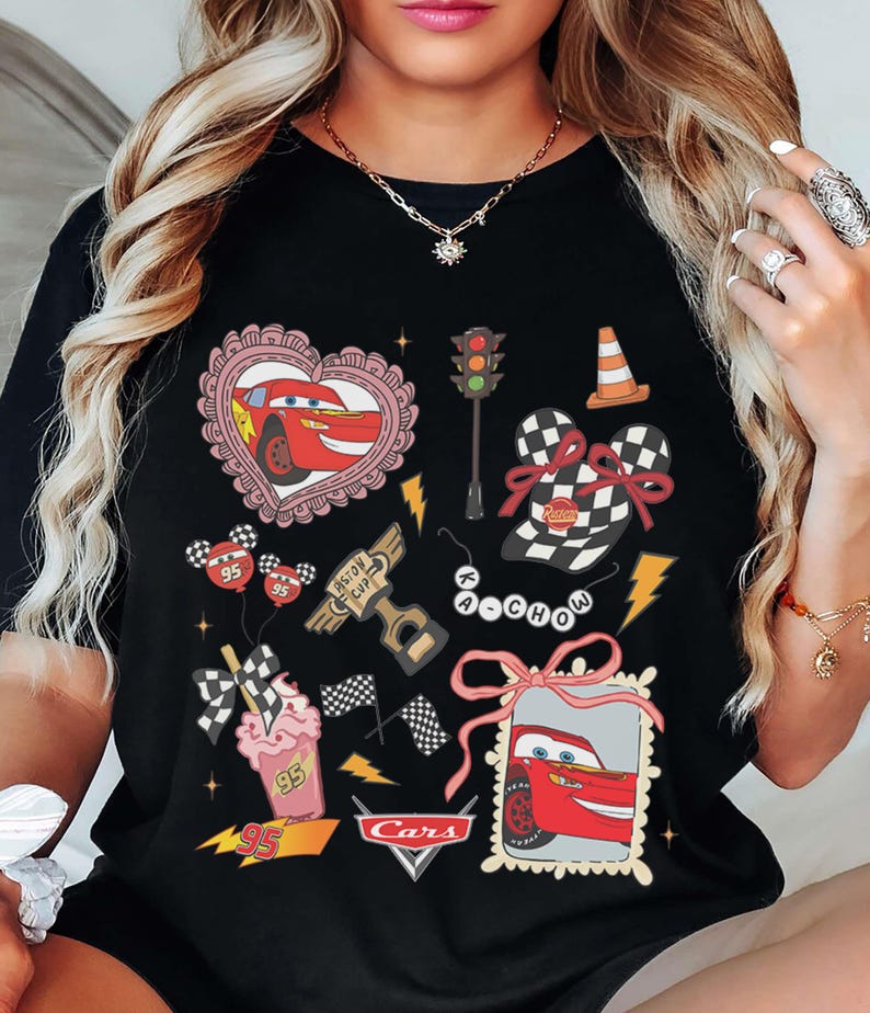 May include: Black t-shirt featuring various Cars movie-themed graphics. Designs include Lightning McQueen in a heart, a traffic light, a cone, checkered flag elements, and the Cars logo. The shirt has a crew neck.