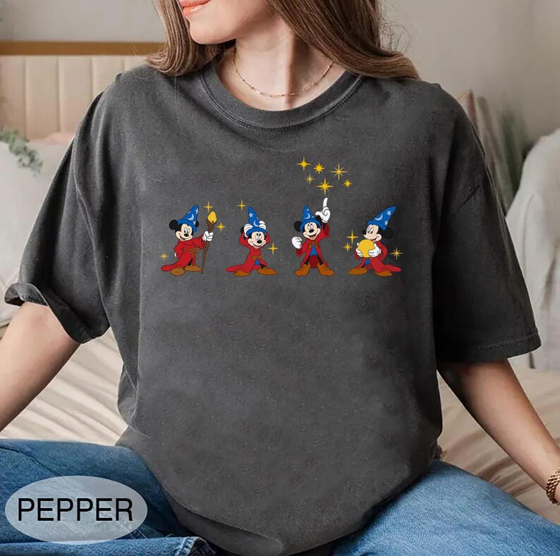May include: Dark gray t-shirt featuring a line of cartoon Mickey Mouse characters dressed as wizards. Each character wears a blue wizard hat and red robe, holding a staff, pointing, or holding a golden orb. The word "PEPPER" is printed at the bottom.