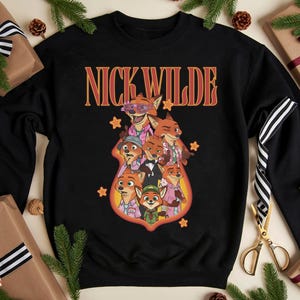 May include: Black crewneck sweatshirt featuring the text "NICK WILDE" in orange and red lettering. The sweatshirt has a graphic of several cartoon foxes in various outfits. The design is surrounded by orange stars.