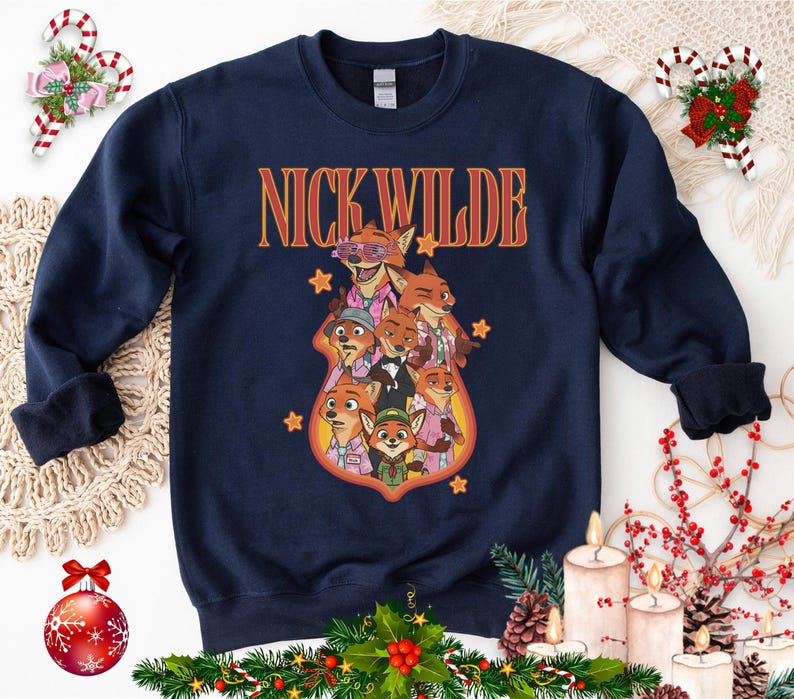 May include: Navy blue sweatshirt featuring a graphic of Nick Wilde and other characters from Zootopia. The text "NICK WILDE" is in orange and yellow. The sweatshirt has a crew neck and long sleeves.