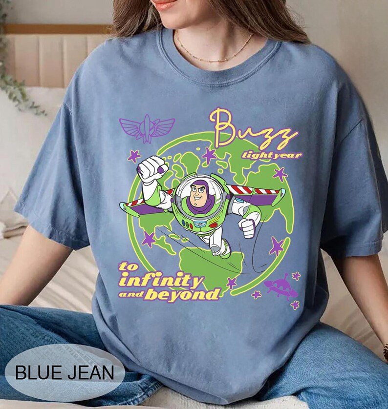 Puede incluir: Una camiseta azul vaquero con un gr&aacute;fico de Buzz Lightyear de Toy Story. El dise&ntilde;o incluye las palabras "Buzz Lightyear" y "to infinity and beyond" en una fuente l&uacute;dica, con estrellas y un gr&aacute;fico de planeta.