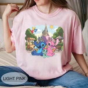 K&ouml;nnte beinhalten: Hellrosa T-Shirt mit einem farbenfrohen Aufdruck von Stitch und Angel, die Eis essen, mit einem Schloss im Hintergrund. Der Text "LIGHT PINK" ist unten auf dem T-Shirt aufgedruckt.