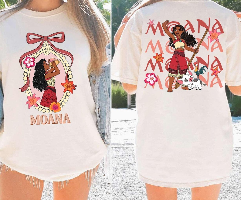 May include: Cream-coloured t-shirt with front and back designs. The front features a cartoon illustration of a woman with the word "MOANA" below. The back displays a similar illustration with the word "MOANA" repeated.