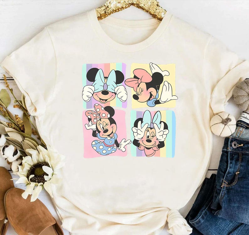 May include: A white t-shirt with a colorful graphic print of four different images of Mickey Mouse. Each image shows Mickey Mouse with a different expression and pose. The background of the graphic is a rainbow.
