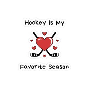 Puede incluir: Una pegatina blanca con el texto "Hockey Is My Favorite Season". El diseño presenta un corazón rojo con palos de hockey cruzados y pequeños corazones rojos alrededor. La pegatina es un diseño divertido y deportivo.