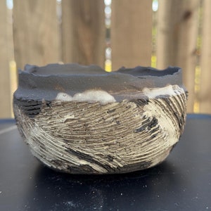 May include: A small, black and white ceramic bowl with a textured, wavy design. The bowl is handmade and has a rustic, earthy feel.