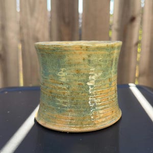 Puede incluir: Un pequeño macetero de cerámica verde y amarillo con un diseño texturizado y rayado.