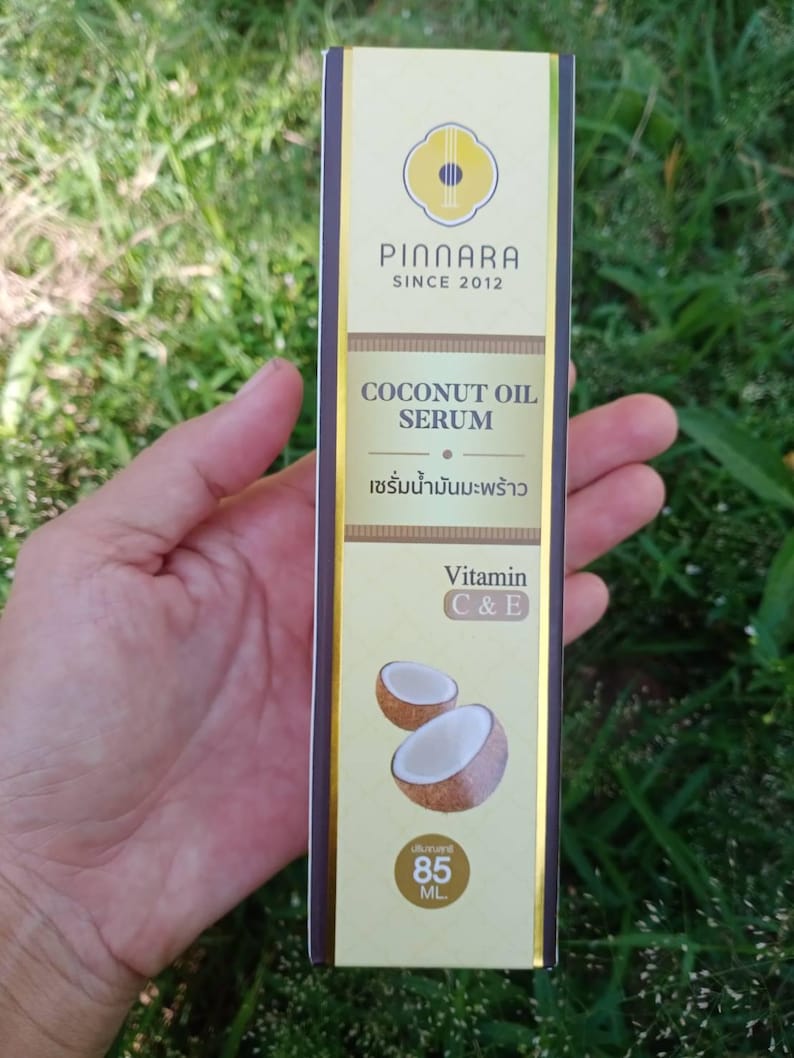 May include: A rectangular box of Pinnara Coconut Oil Serum. The box is primarily gold with brown accents and features the brand name and product details. The text includes "COCONUT OIL SERUM" and "Vitamin C & E". The box also shows a graphic of two coconut halves and contains 85 ML.