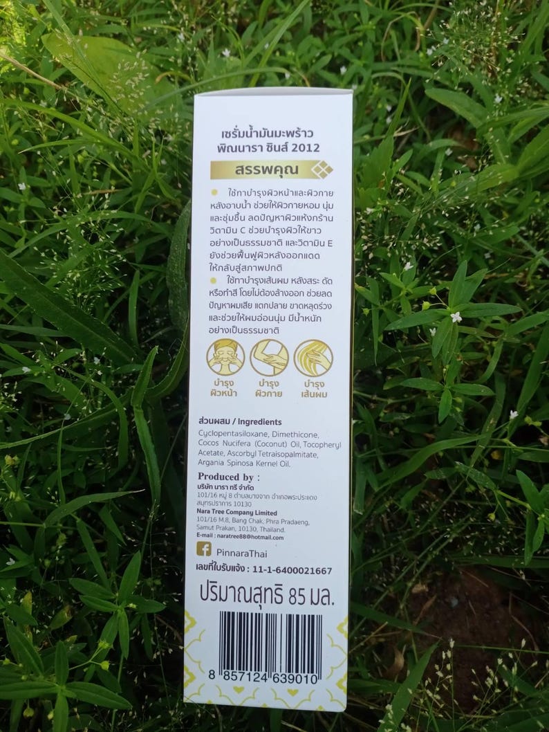 May include: A white product box with text in Thai, featuring a gold emblem and product details. The box lists ingredients and instructions for use, including hair and skin care benefits. The product volume is 85 ml.