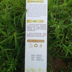 May include: A white product box with text in English and Chinese, set against a backdrop of green foliage. The box details the product's purpose, including nourishing skin and hair. The text "Made in Thailand" is also visible.