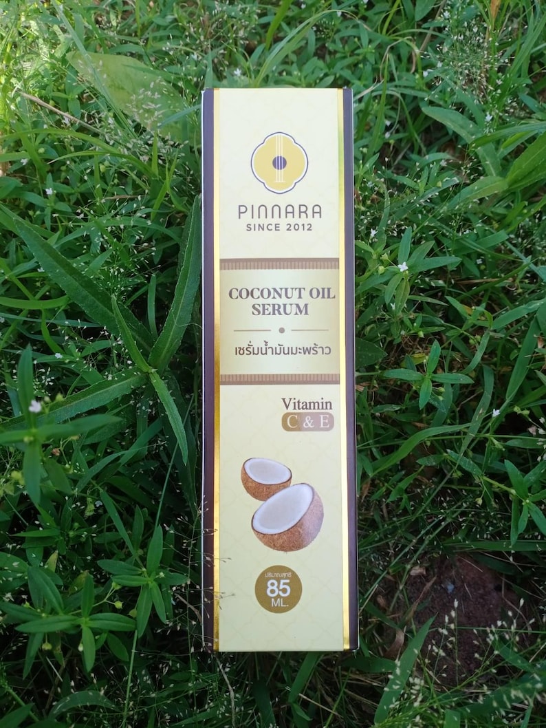 May include: A rectangular box of Pinnara Coconut Oil Serum, with text in English and Thai. The box is cream and brown, with a logo and the words "COCONUT OIL SERUM". It also features images of coconuts and states the serum contains Vitamin C & E. The box contains 85 mL.