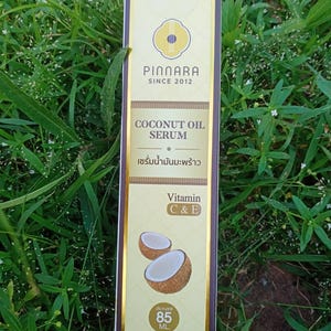 May include: A rectangular box of Pinnara Coconut Oil Serum. The box is primarily beige with gold accents and features the brand name and product details. The text "COCONUT OIL SERUM" is visible, along with "Vitamin C & E" and an image of a coconut. The box contains 85 mL.