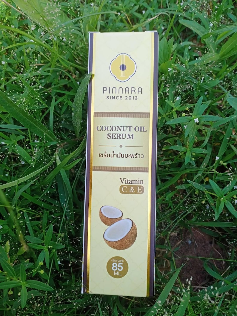 May include: A rectangular box of Pinnara Coconut Oil Serum. The box is primarily beige with gold accents and features the brand name and product details. The text "COCONUT OIL SERUM" is visible, along with "Vitamin C & E" and an image of a coconut. The box contains 85 mL.