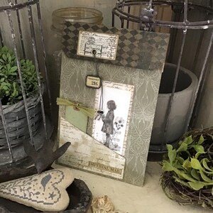 May include: A decorative paper folder featuring a sage green damask pattern, a dark brown diamond-checkered top border, and a vintage-style illustration of a child. It includes a small tag labeled 216 and a bottom label reading IMPERIAL MAIL.