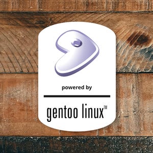 Puede incluir: Una pegatina blanca con un logotipo morado y el texto "powered by gentoo linux" está adherida a una superficie de madera. El logotipo es una forma estilizada y curvada. La madera tiene un aspecto natural y rústico.