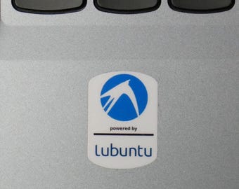 May include: A white sticker with a blue logo and the text "powered by Lubuntu" is affixed to a silver laptop. The logo features a stylized bird within a blue circle. The sticker is rectangular with rounded corners.