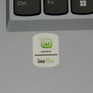 May include: A white sticker with the Linux Mint logo, a stylized green 'M' inside a square, and the words 'powered by' above a horizontal line. Below the line is the text 'Linux Mint' in green.