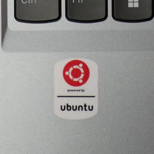 May include: A white sticker with a red and white Ubuntu logo, and the text "powered by" above the word "ubuntu" in black. The sticker is on a silver laptop surface.