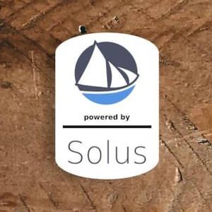May include: A white, blue, and navy logo with a sailboat design, set against a brown background. The text "powered by" is above a horizontal line, with the name "Solus" below in a sans-serif font.