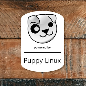 May include: A white oval sticker with a cartoon dog face logo. The text "powered by" is above a horizontal black line, with "Puppy Linux" written below in a sans-serif font. The background is a wooden surface.