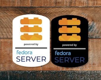 Può includere: Due adesivi rettangolari con angoli arrotondati, uno bianco e uno nero. Entrambi presentano tre forme geometriche arancioni impilate, la scritta "powered by" sopra una linea orizzontale e il testo blu "fedora SERVER" posizionato sotto.