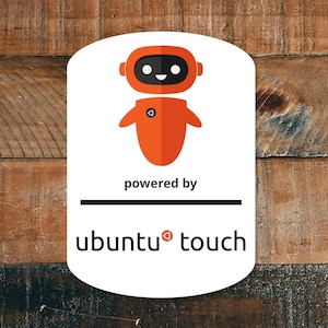Puede incluir: Una pegatina blanca con un diseño de robot naranja y el texto "powered by ubuntu touch". El robot tiene una cara negra y un pequeño diseño circular en el pecho. La pegatina está sobre un fondo de madera.