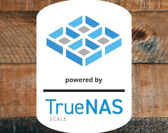 May include: A white rectangular sticker with rounded corners featuring a blue and grey geometric logo at the top. Below the logo, the text reads "powered by" in black, followed by a horizontal line and the blue text "TrueNAS SCALE".