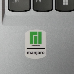May include: A white sticker with a green and white logo and the text "powered by" above the word "manjaro" in a sans-serif font. The sticker is on a silver laptop surface, near the Ctrl and Fn keys.