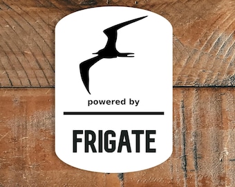May include: A white, rounded rectangle featuring a black bird silhouette. The text "powered by" appears above the word "FRIGATE" in bold, black letters. Set against a textured, brown wooden background.
