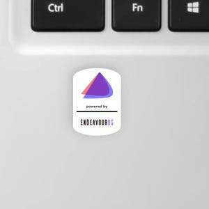 May include: A white sticker featuring a purple and red triangle design, with the text "powered by" and "ENDEAVOUROS" in black. The sticker is placed on a white laptop surface, near the Ctrl and Fn keys.