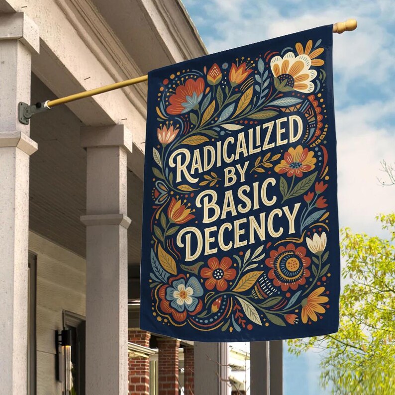 May include: A navy blue house flag with the words "RADICALIZED BY BASIC DECENCY" in a decorative font. The flag features a floral design in orange, yellow, and blue. The flag is hanging from a gold-coloured pole.