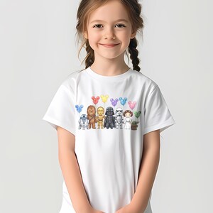 Puede incluir: Camiseta blanca con un gr&aacute;fico colorido de personajes de Star Wars y globos con forma de Mickey Mouse. El dise&ntilde;o incluye a R2-D2, Chewbacca, C-3PO, Darth Vader, un Stormtrooper, la Princesa Leia y Grogu.