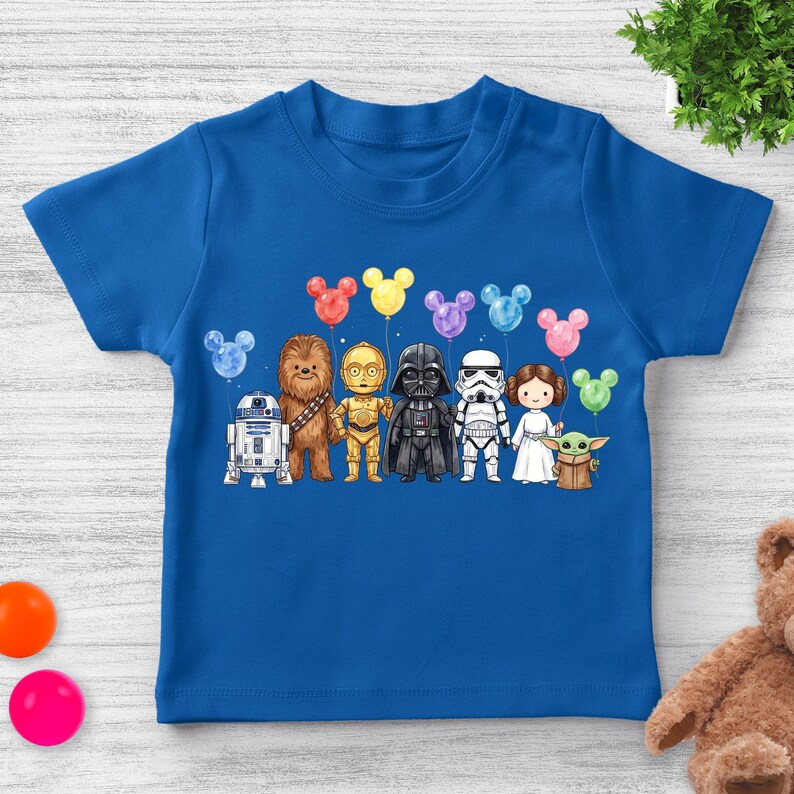 Puede incluir: Una camiseta azul con una ilustraci&oacute;n de personajes de Star Wars sosteniendo globos con forma de Mickey Mouse. Los personajes incluyen a R2-D2, Chewbacca, C-3PO, Darth Vader, un Stormtrooper, la Princesa Leia y Grogu.